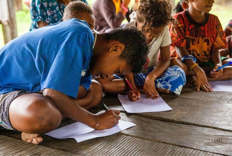 A boy writing whilst leaning on the floor